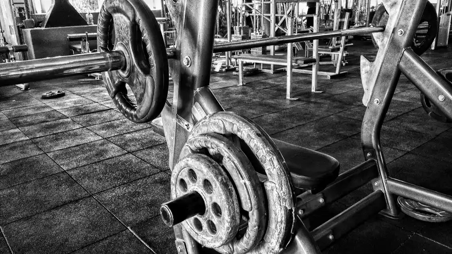 A member pressing a barbell on a bench press station in a commercial gym